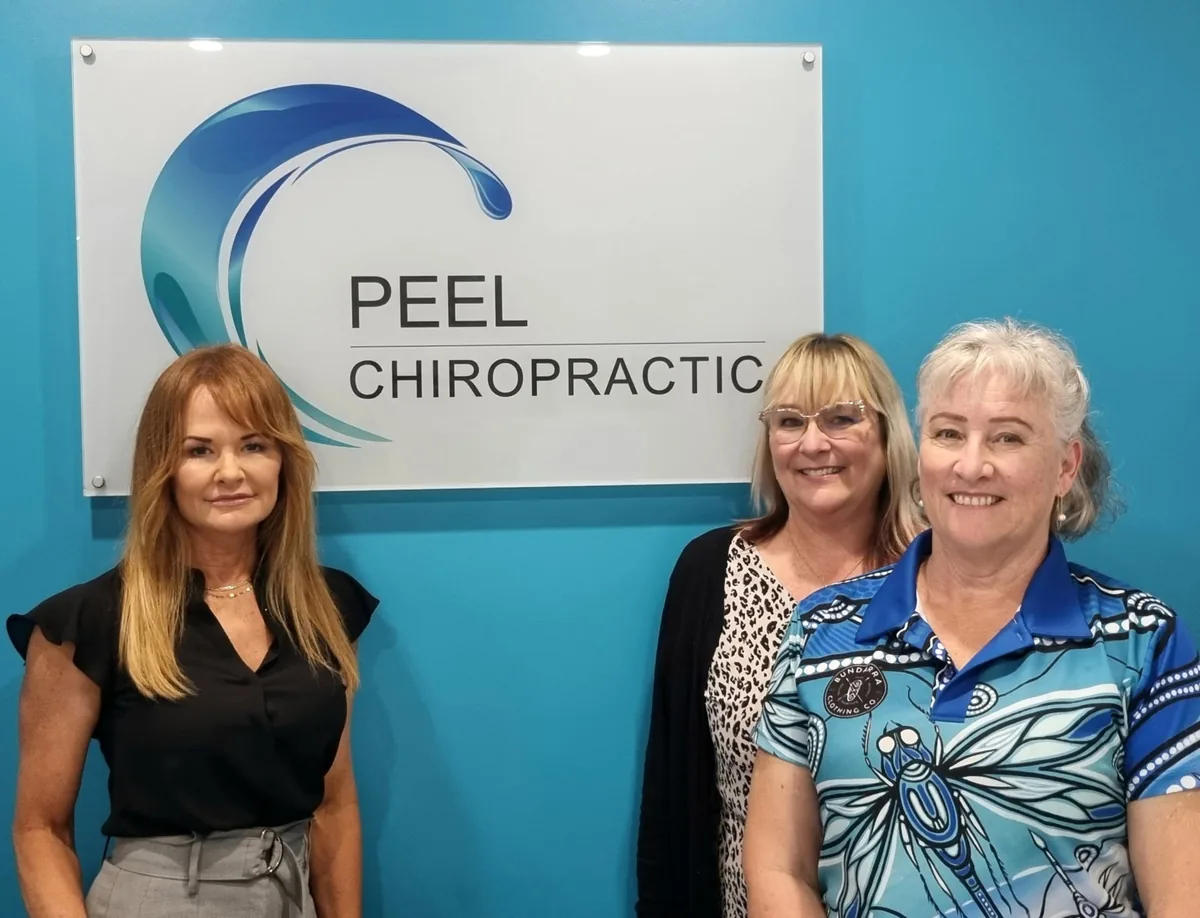 Three of our chiropractic assistants in front of the Peel Chiropractic sign at the clinic