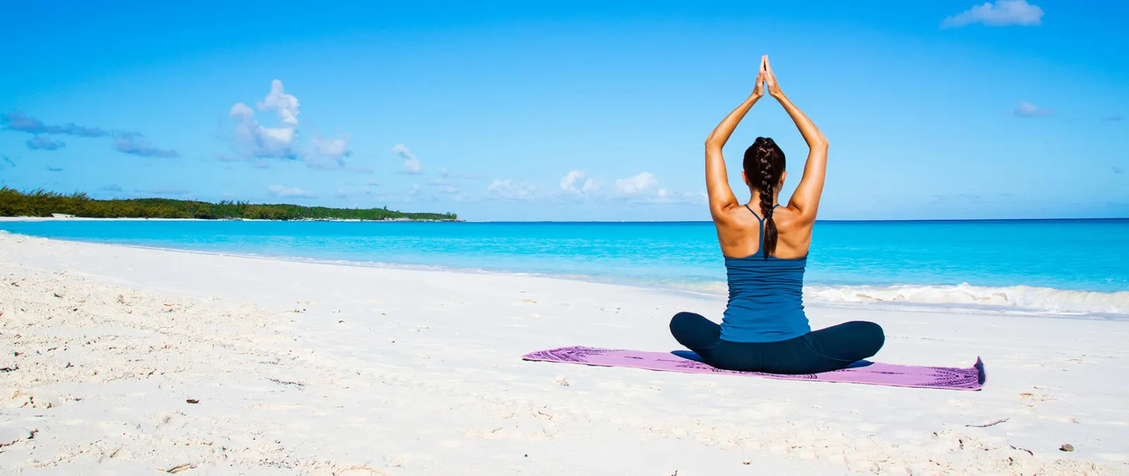 A woman doing yoga on a white sand beach