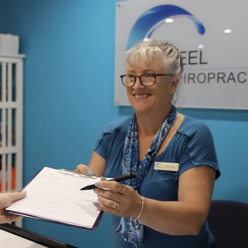 A Peel Chiropractic assistant hands a new patient the paperwork on a clipboard at reception